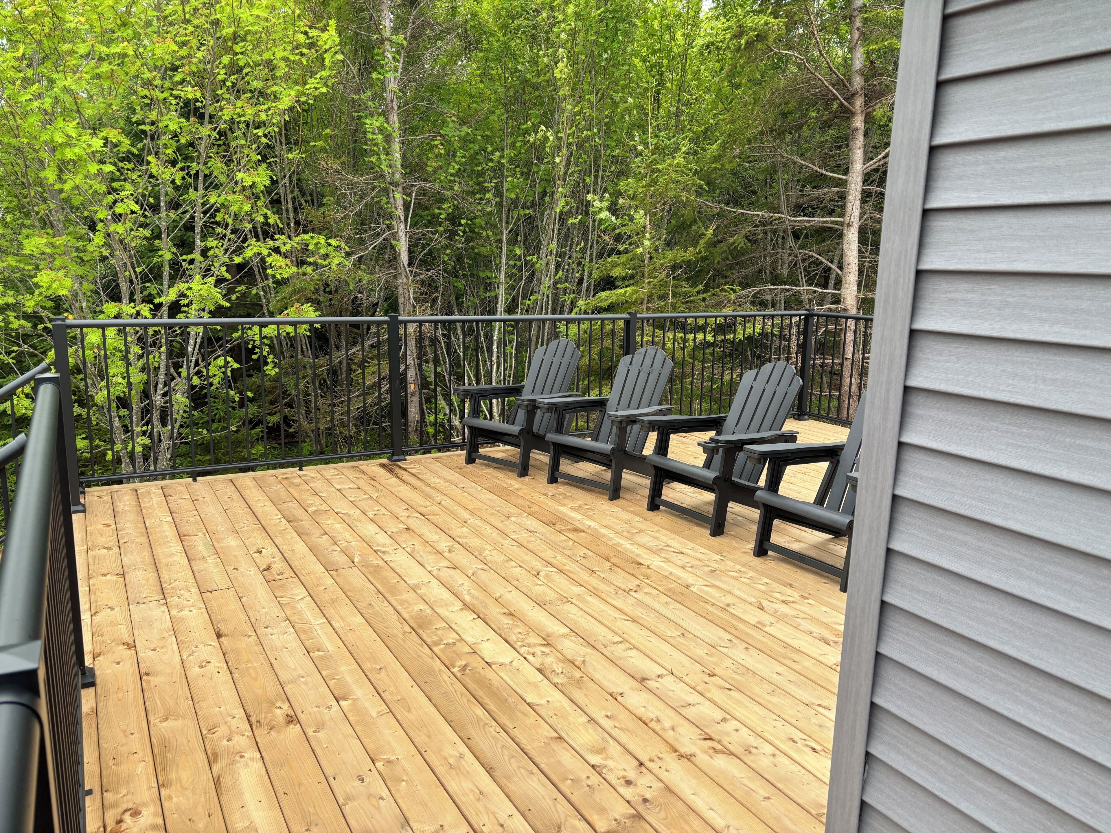 Une terrasse en bois avec trois fauteuils Adirondack, entourée d’arbres.