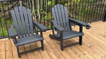 Dos sillas Adirondack en una terraza de madera con baranda de metal, rodeadas de árboles.