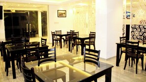 A dining area with multiple tables and chairs, a glass partition, and patterned wall decor. - Hotel Sky Gate Kandy  (Kandy)