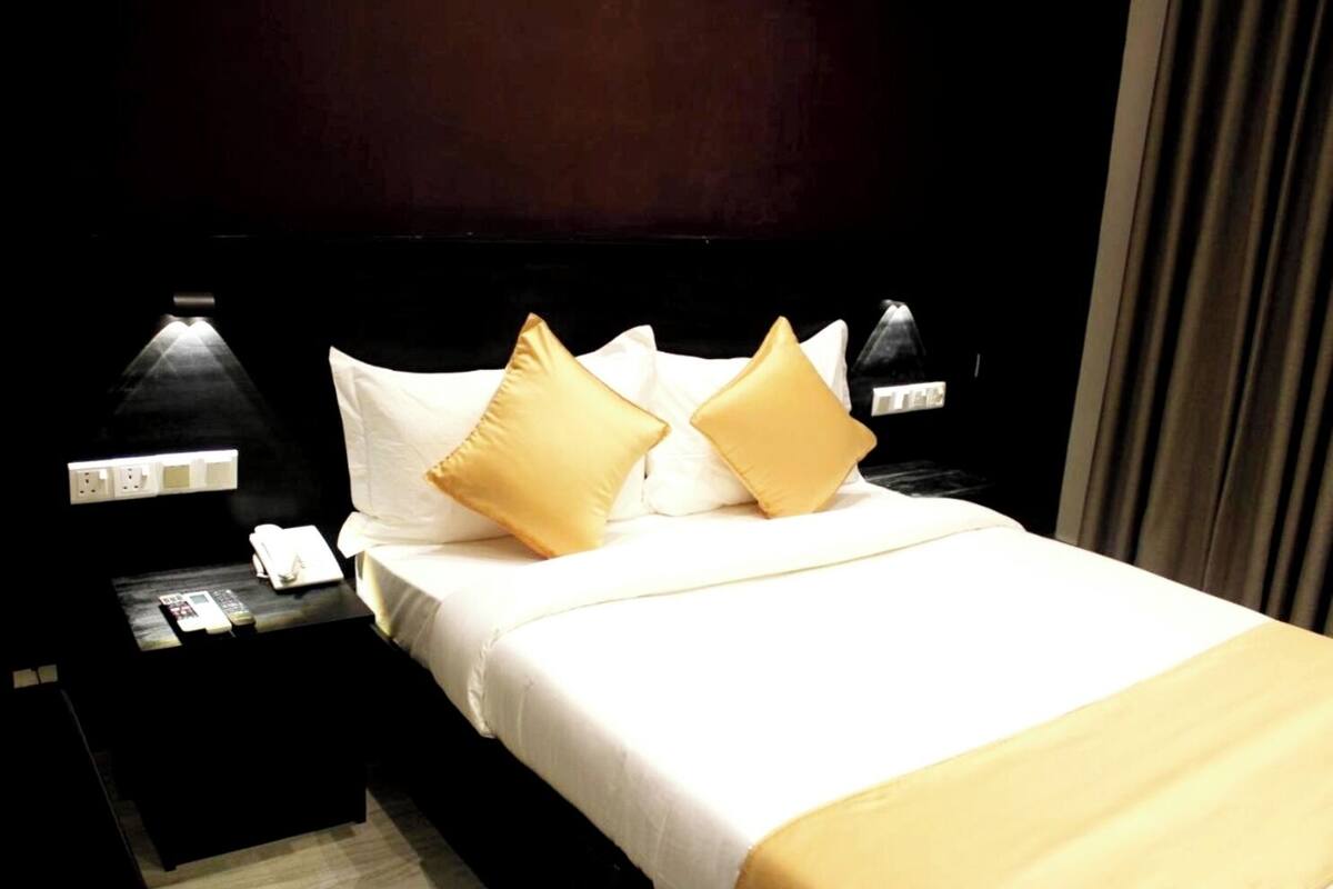 Una camera d'albergo con un letto rifatto, due comodini con lampade e un tavolino con telefono e telecomando.