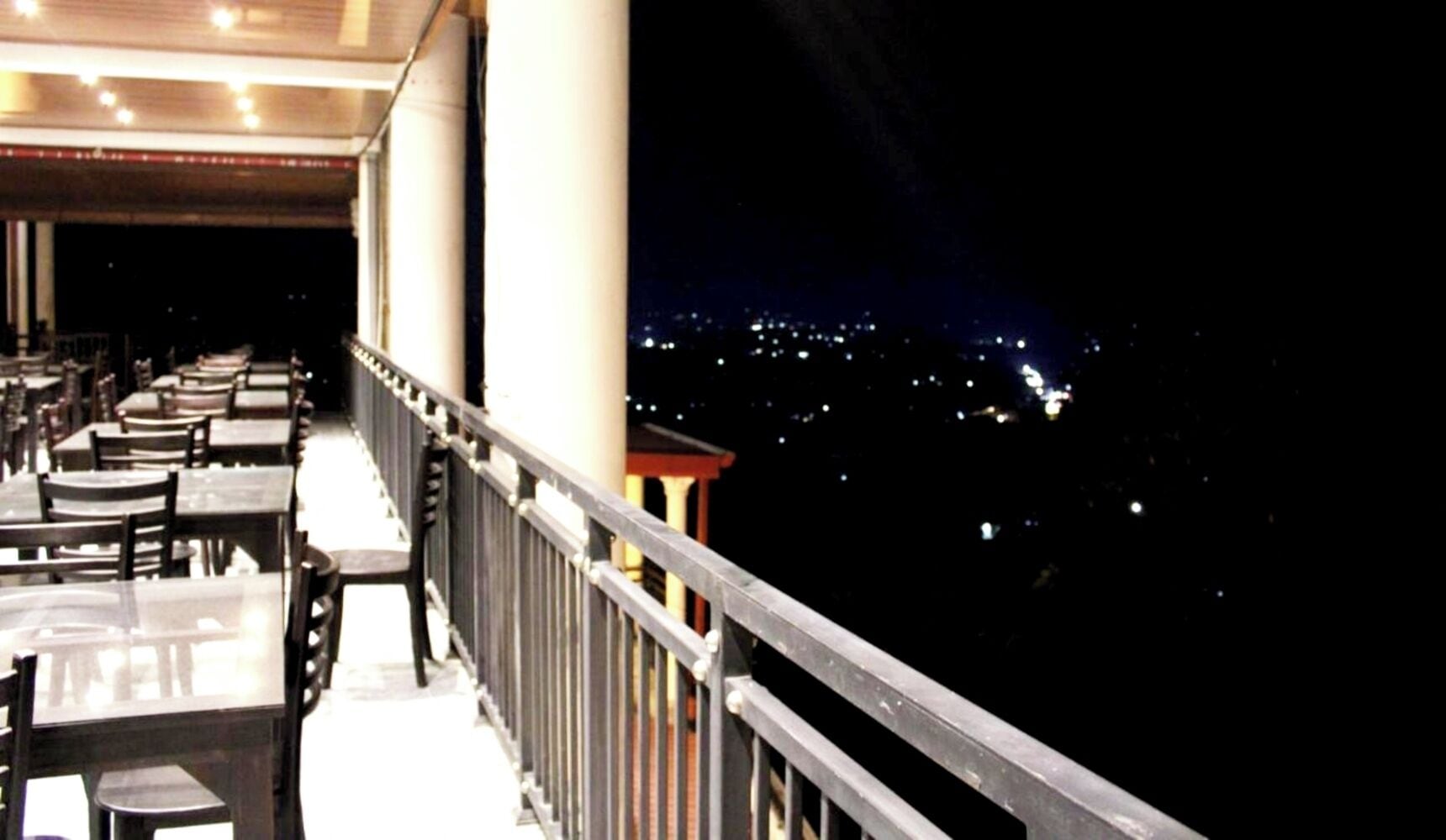 A restaurant with tables and chairs arranged along a balcony with a railing.