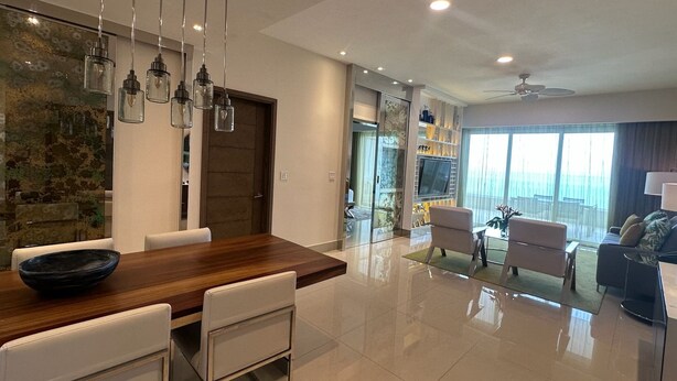 Una sala de estar moderna con una mesa de comedor de madera, sillas blancas, un sofá y un televisor montado en la pared.