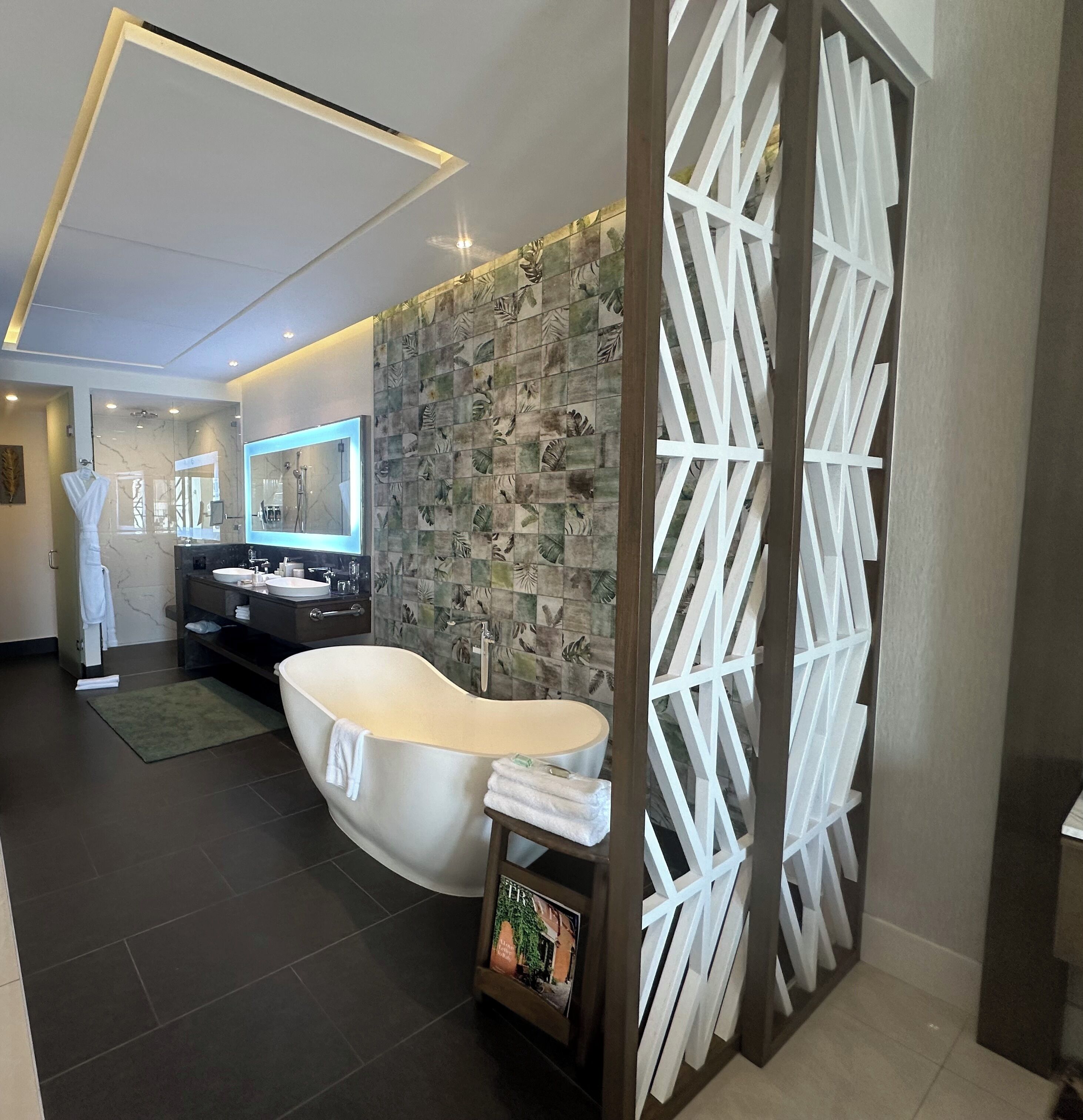 A modern bathroom with a freestanding bathtub, a vanity with a mirror, and a decorative wall with leaf patterns.