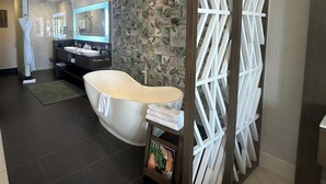 Un baño moderno con una bañera independiente, un tocador con espejo y una pared decorativa con motivos de hojas.
