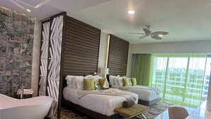 Una habitación de hotel moderna con una cama grande, dos mesitas de noche, una zona de estar, una bañera y un ventanal con cortinas.