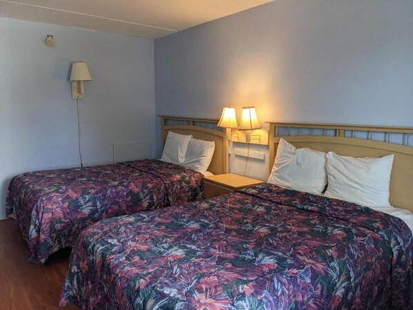 A hotel room with two beds, each with floral-patterned bedding, a nightstand, and two wall-mounted lamps. - Beach Side Hotel (Myrtle Beach)
