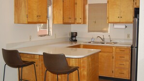 A kitchen with wooden cabinets, a large island with two bar stools, a coffee maker, and a refrigerator. - The Casita at Lizard Gate is a 1-bedroom guest house in mid-town Tucson. (Tucson)