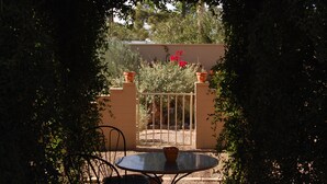 A patio with a round table and chairs, surrounded by greenery and a gate leading to a garden. - The Casita at Lizard Gate is a 1-bedroom guest house in mid-town Tucson. (Tucson)