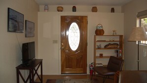 A living room with a wooden door, a television on a stand, a bookshelf, a chair, and a lamp. - The Casita at Lizard Gate is a 1-bedroom guest house in mid-town Tucson. (Tucson)