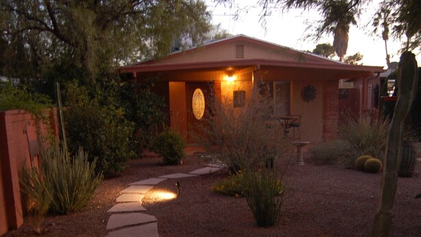 A pathway leading to a house with a red roof, surrounded by desert plants and a gravel driveway. - The Casita at Lizard Gate is a 1-bedroom guest house in mid-town Tucson. (Tucson)