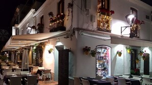 Ein Restaurant mit Außenbereich, Tischen, Stühlen und einer überdachten Sitzgelegenheit, beleuchtet mit dekorativen Lichtern.