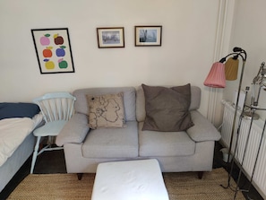 A room with a grey sofa, a white bench, a blue chair, and a radiator. There are two framed pictures on the wall. - Modern Studio-Apartment Close to Stockholm (Stockholm)