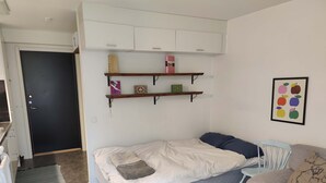 Una habitación pequeña con cama, una silla, un sofá y estantes empotrados con objetos.