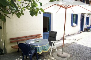 A small outdoor seating area with a round table, two chairs, a bench, and a white umbrella.