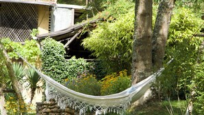 A hammock in a lush garden with a stone wall and a wooden structure in the background. - Charming Old Farmhouse in Secluded Nature – Perfect for Family & Friends (Sédeilhac)