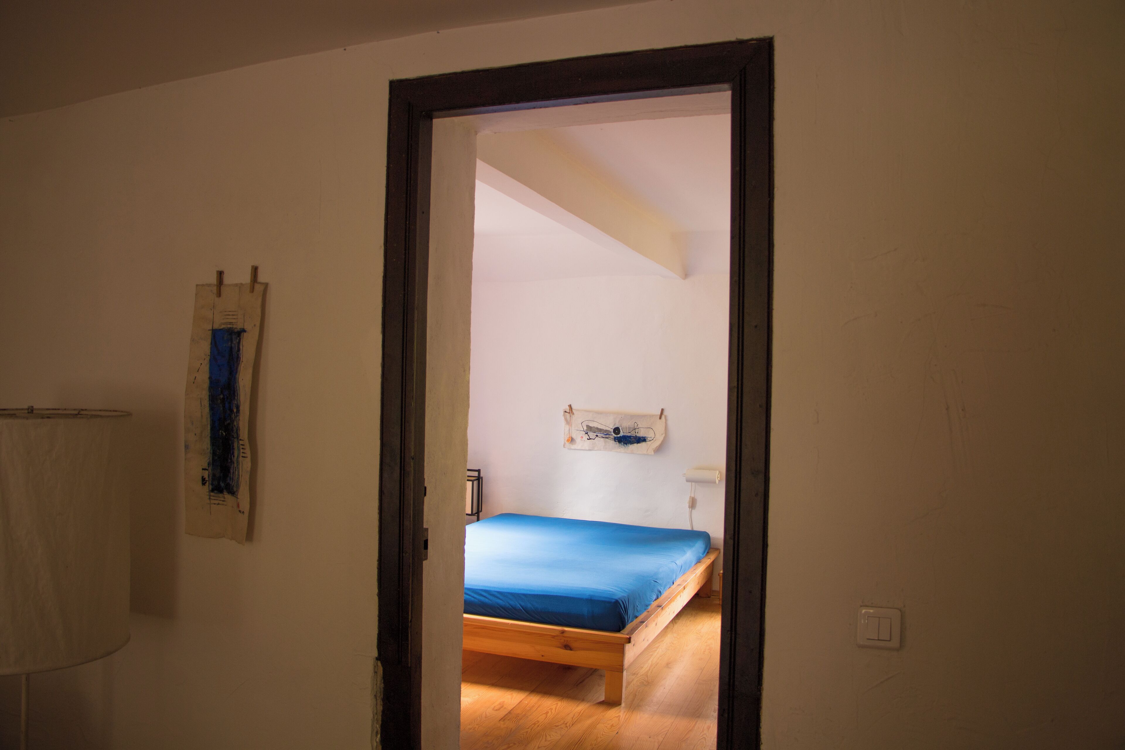 Una habitación con una cama de madera, una pared blanca y una puerta que da a otra estancia.