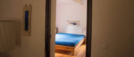 Una habitación con una cama de madera, una pared blanca y una puerta que da a otra estancia.
