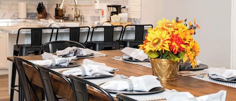 Un comedor con una mesa de madera dispuesta para seis personas, rodeada de sillas negras. Un jarrón con girasoles está sobre la mesa.