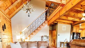 A spacious living room with a wooden ceiling, a leather sofa, a coffee table, and a staircase with a wrought iron railing. - Family Friendly 3 Bear Cubs Cabin-Buck Mtn-EV Charger,AC,Views (Purlear)
