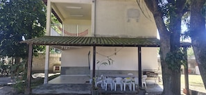 A covered outdoor seating area with a tiled roof, a number 279 sign, and white plastic chairs.
