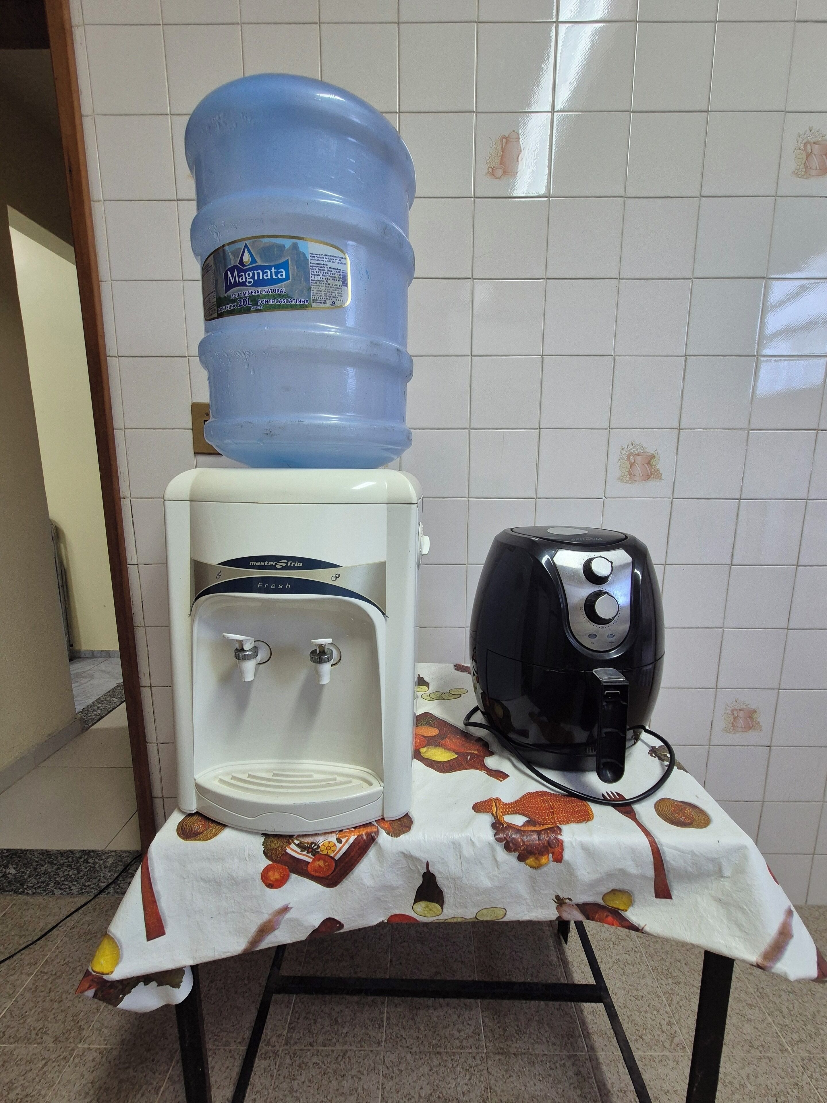 Un dispensador de agua y un tostador sobre una mesa con mantel.
