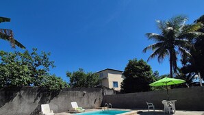 Uma piscina com um deck de concreto, algumas cadeiras de descanso e um guarda-sol verde.