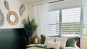 Quarto com colcha verde, um espelho grande e janela com persianas.