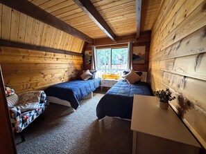 Eine Hütte mit zwei Betten, einem kleinen Tisch und einem Fenster mit Blick ins Freie.