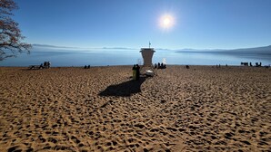 Una playa con una torre de salvavidas, cielos despejados y agua tranquila.