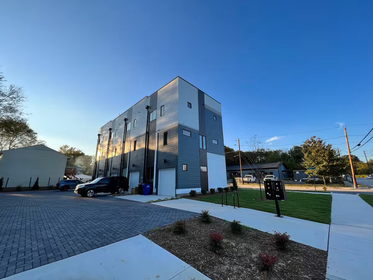 A modern multi-story building with a parking area, a covered parking structure, and a well-maintained lawn.