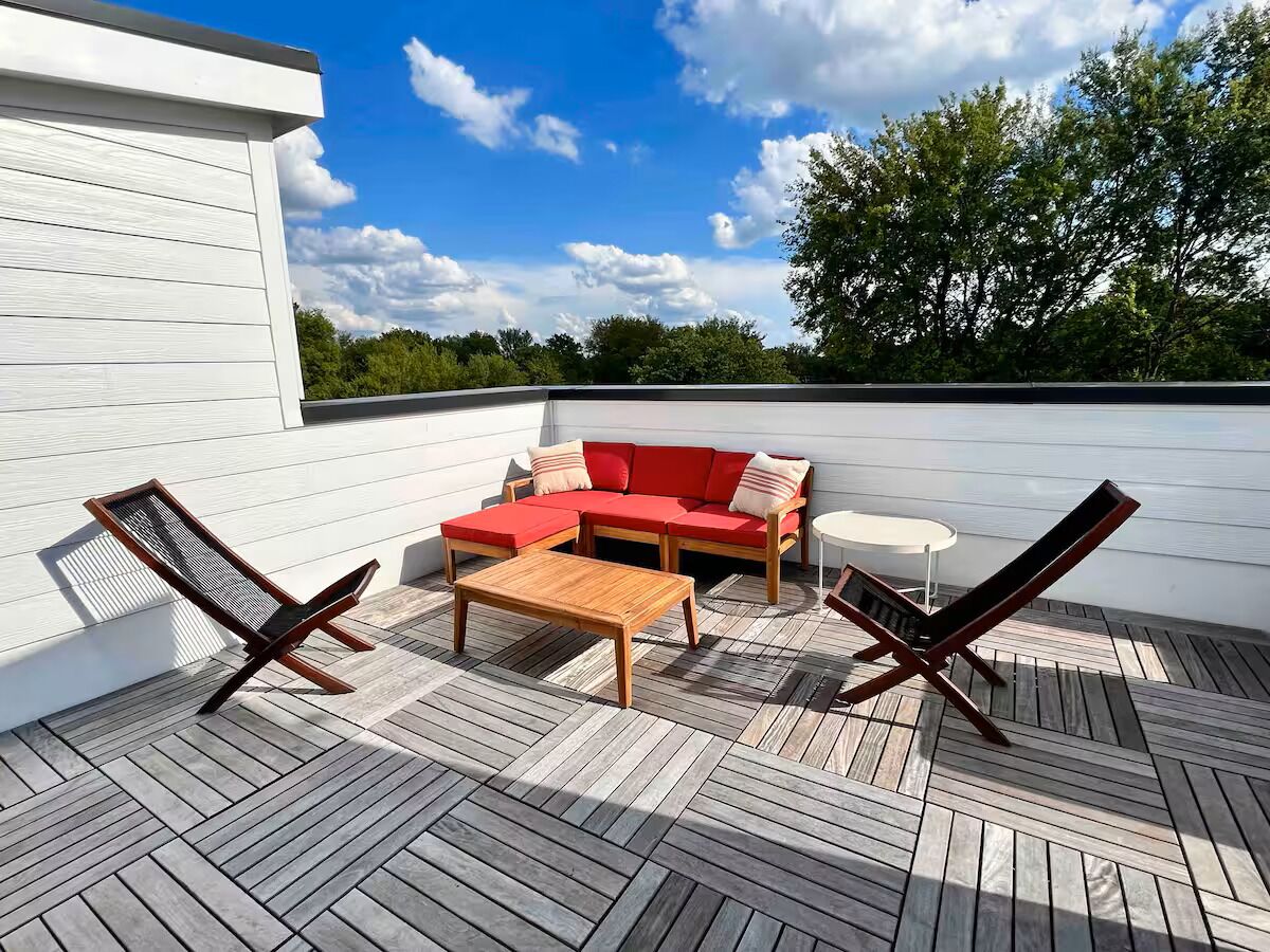 A rooftop patio with a wooden deck, a red sofa, two lounge chairs, and a small table.