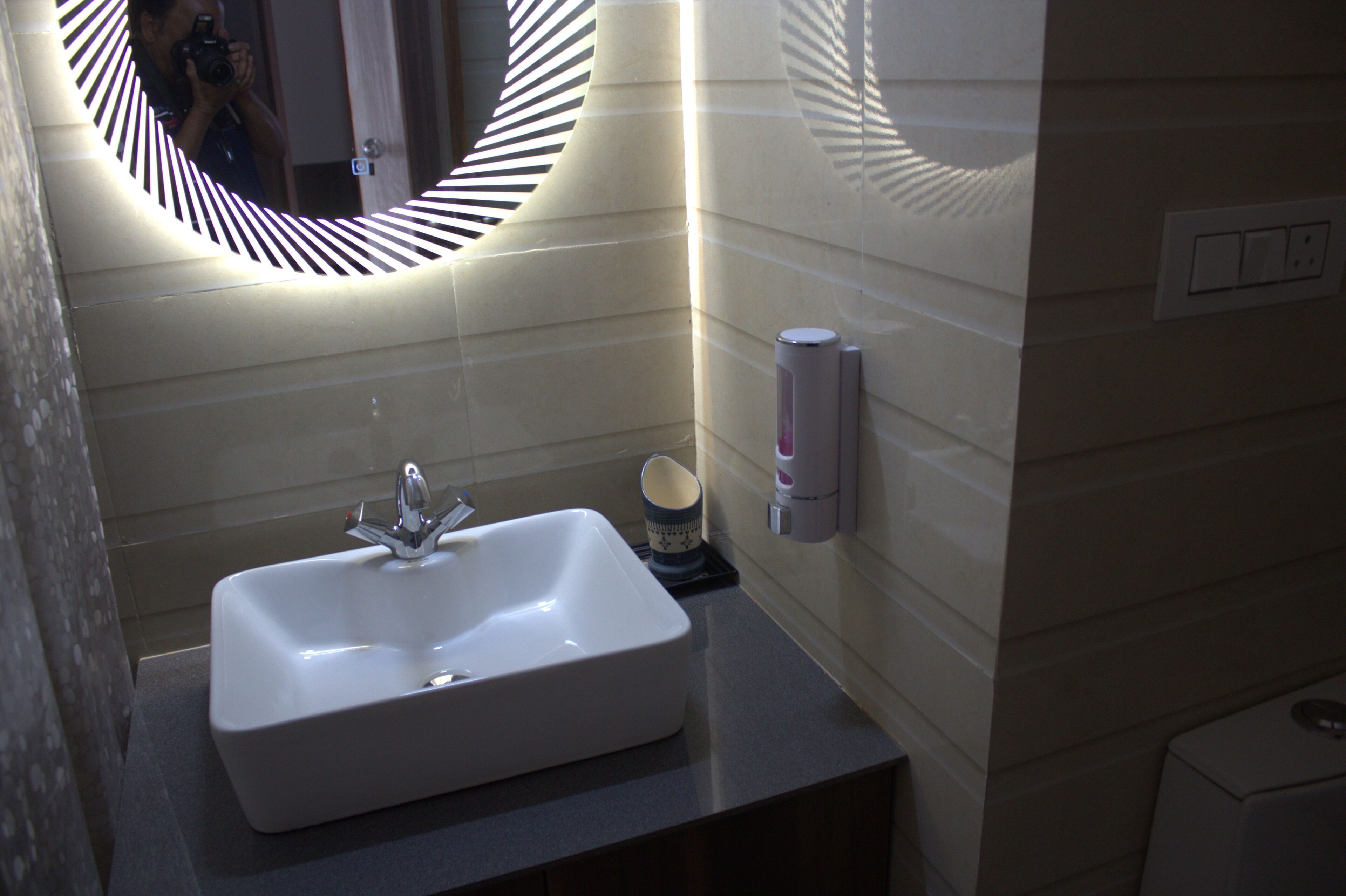 A bathroom with a white sink, a mirror with a striped frame, and a soap dispenser on the wall.