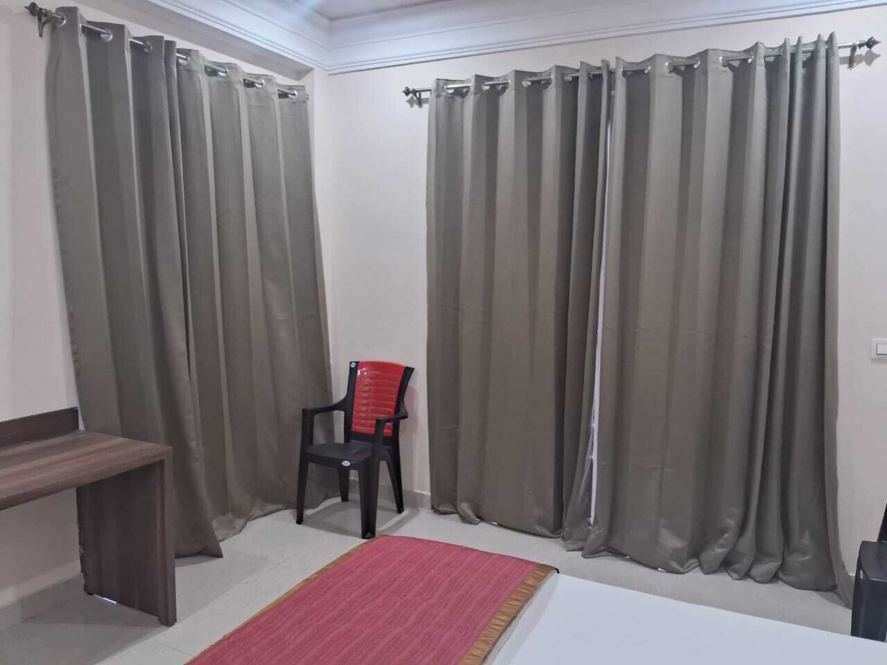 A room with two curtains, a chair, a small table, and a red rug.