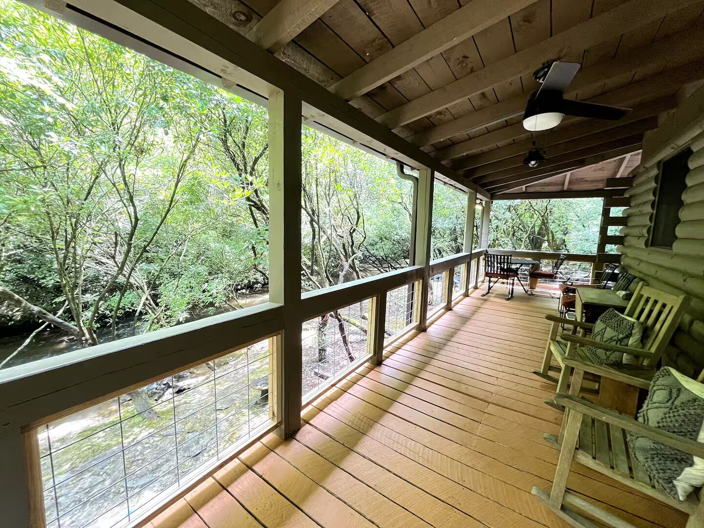 A wooden deck with a railing, overlooking a forested area with a stream.