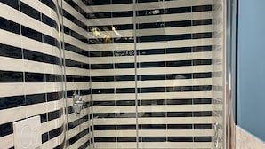 Een badkamer met een douchecabine van glas, een toilet en gestreepte wandtegels.
