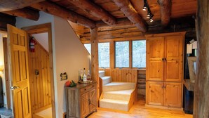 Een houten interieur met een trap, houten kasten en een raam met uitzicht op bomen.