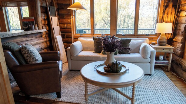 Een gezellig interieur van een blokhut met een bank, fauteuil en een ronde salontafel met decoratieve objecten.