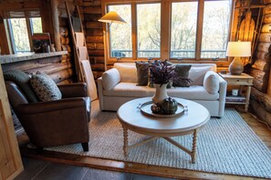 A cozy log cabin interior with a sofa, armchair, and a round coffee table with decorative items. - Hidden Willow Cabin - Lake Sunapee Region (Newbury)