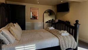 A neatly made bed with a headboard, a bedside table, and a wall-mounted TV. - The Five Bells Inn (Claypole)