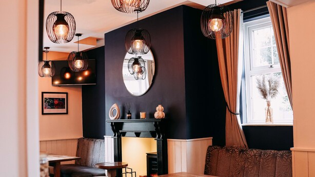 A cozy dining area with a wooden table and benches, a fireplace, and pendant lighting. - The Five Bells Inn (Claypole)