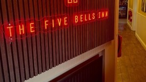 A hotel interior with a neon sign reading "THE FIVE BELL'S INN" and a vertical wooden panel design. - The Five Bells Inn (Claypole)