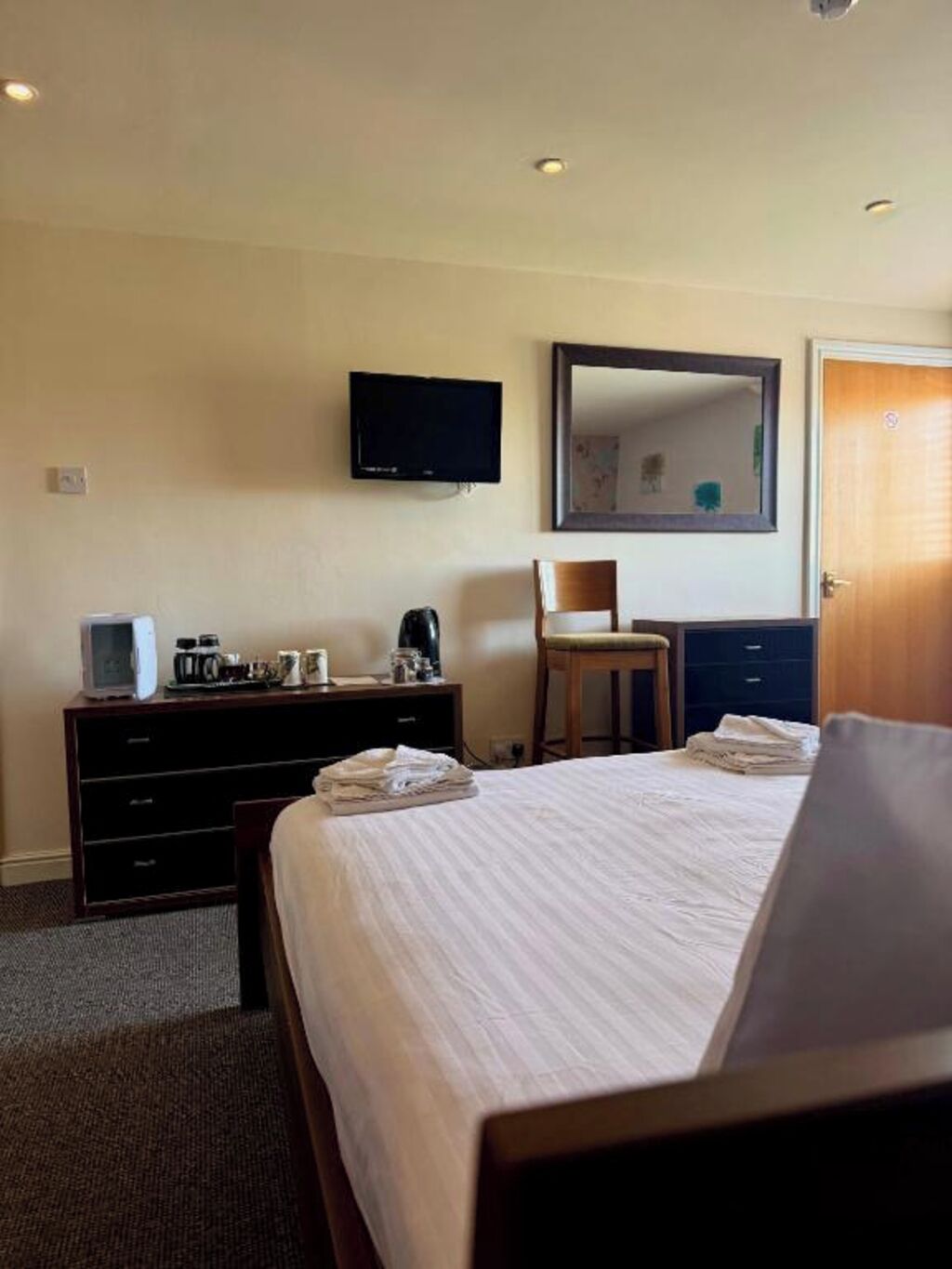 A hotel room with a bed, a dresser, a television mounted on the wall, and a door.