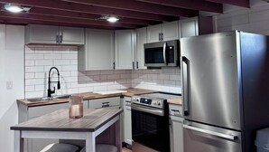 A modern kitchen with white cabinets, a stainless steel refrigerator, a microwave, and an oven. There is a wooden countertop and a bar stool. - Charming Vintage Home w/Separate Barn Guesthouse and Yard (San Antonio)