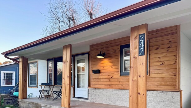 A modern house with a wooden facade, a front porch with a table and chairs, and a mailbox. - Charming Vintage Home w/Separate Barn Guesthouse and Yard (San Antonio)