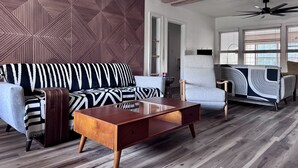A modern living room with a geometric patterned wall, a sofa with striped cushions, a wooden coffee table, and a chair with a black and white abstract design. - Charming Vintage Home w/Separate Barn Guesthouse and Yard (San Antonio)