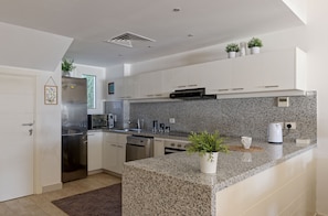 A modern kitchen with white cabinets, granite countertops, stainless steel appliances, and potted plants. - VESTA - Luxury Villa - 4BR - Joubal (El Gouna)