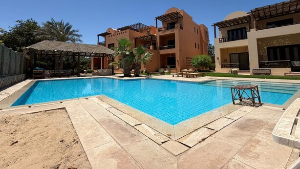 Una piscina rodeada de edificios con balcones y un área de estar cubierta.