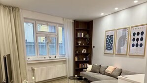 Ein modernes Wohnzimmer mit einem Glastisch, grünen Stühlen, einem grauen Sofa und einem Bücherregal.