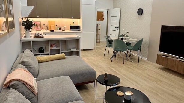 Ein modernes Wohnzimmer mit einem grauen Ecksofa, einem kleinen schwarzen Couchtisch und einem Fernseher auf einem Holzgestell.