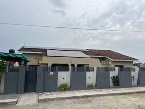 Une maison moderne à deux étages, dotée d’une clôture grise, de panneaux solaires et d’un toit recouvert de tuiles.